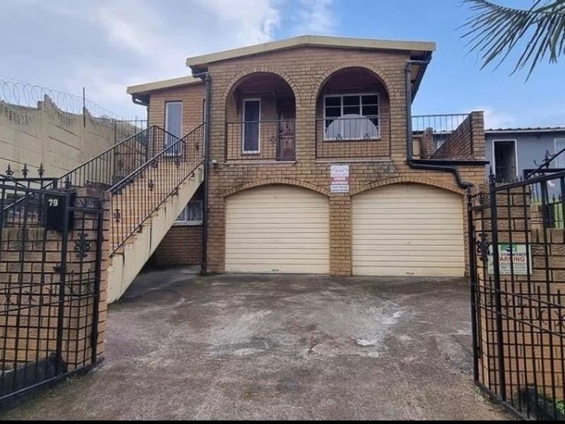 Front elevation of a double-story brick house featuring a double garage, external staircase leading to an upper balcony, and secure gated entrance.