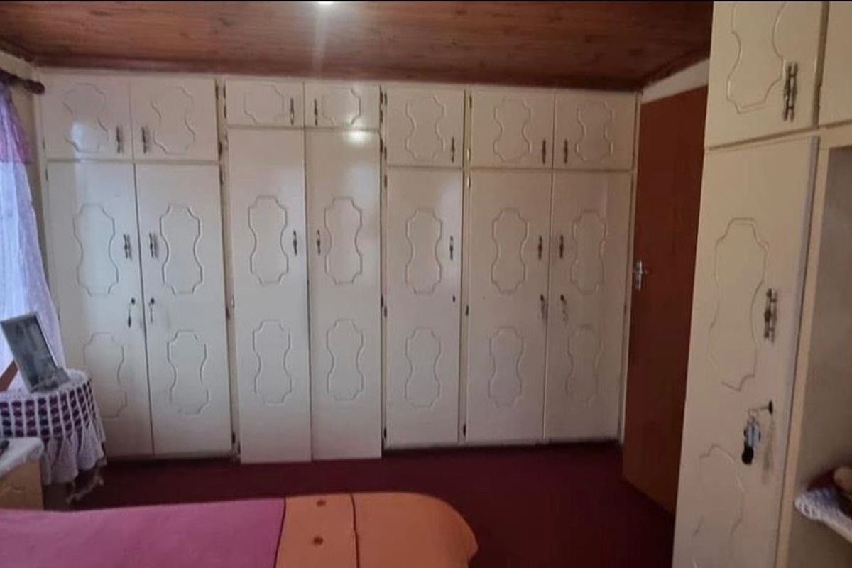 Bedroom featuring extensive built-in cabinetry, a timber-clad ceiling, and fitted vanity unit, offering significant storage potential in a dated interior setting.