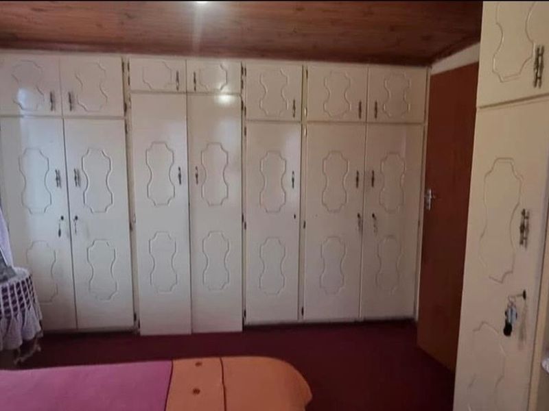 Bedroom featuring extensive built-in cabinetry, a timber-clad ceiling, and fitted vanity unit, offering significant storage potential in a dated interior setting.