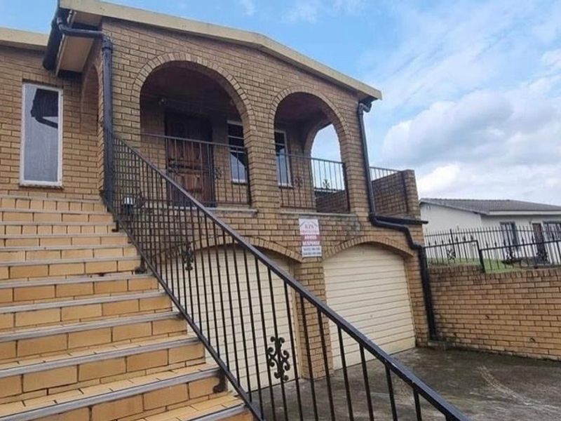 A double-story face brick home featuring an arched balcony, external tiled staircase with wrought iron railings, and a double garage.