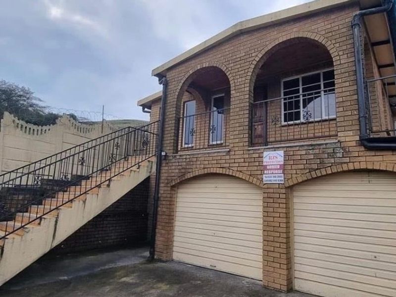 Front view of a double-story brick house featuring a double garage, an external staircase with iron railings, and an upper-level balcony.