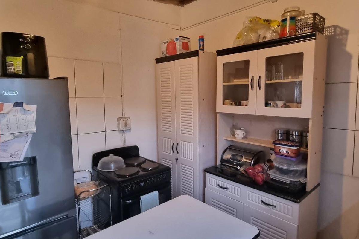 A functional kitchen area featuring tiled splashbacks, built-in cabinetry, and a freestanding stove, offering potential for modernization and aesthetic improvement.
