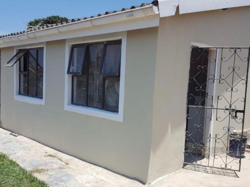 Rear exterior view of the house featuring neutral painted walls, aluminium window frames, and a metal security gate.