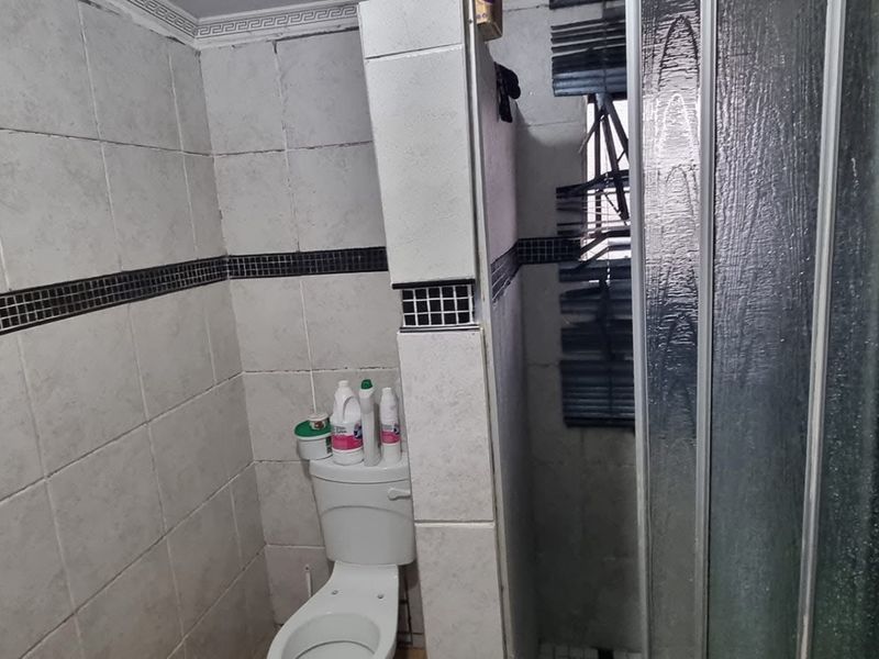 A functional bathroom featuring a shower enclosure, toilet, and tiled walls with a decorative border, requiring cosmetic updates to improve its overall condition.