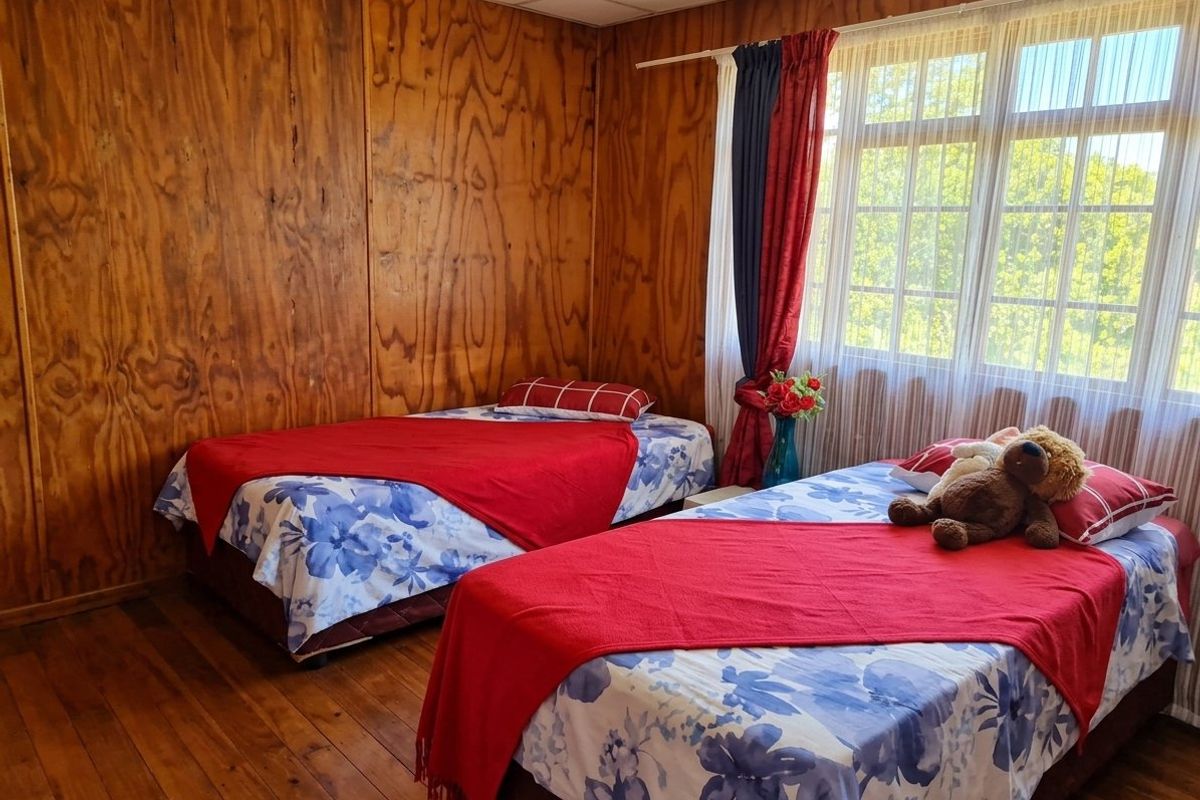 A bedroom featuring wood-paneled walls, timber flooring, and a large window providing natural light.