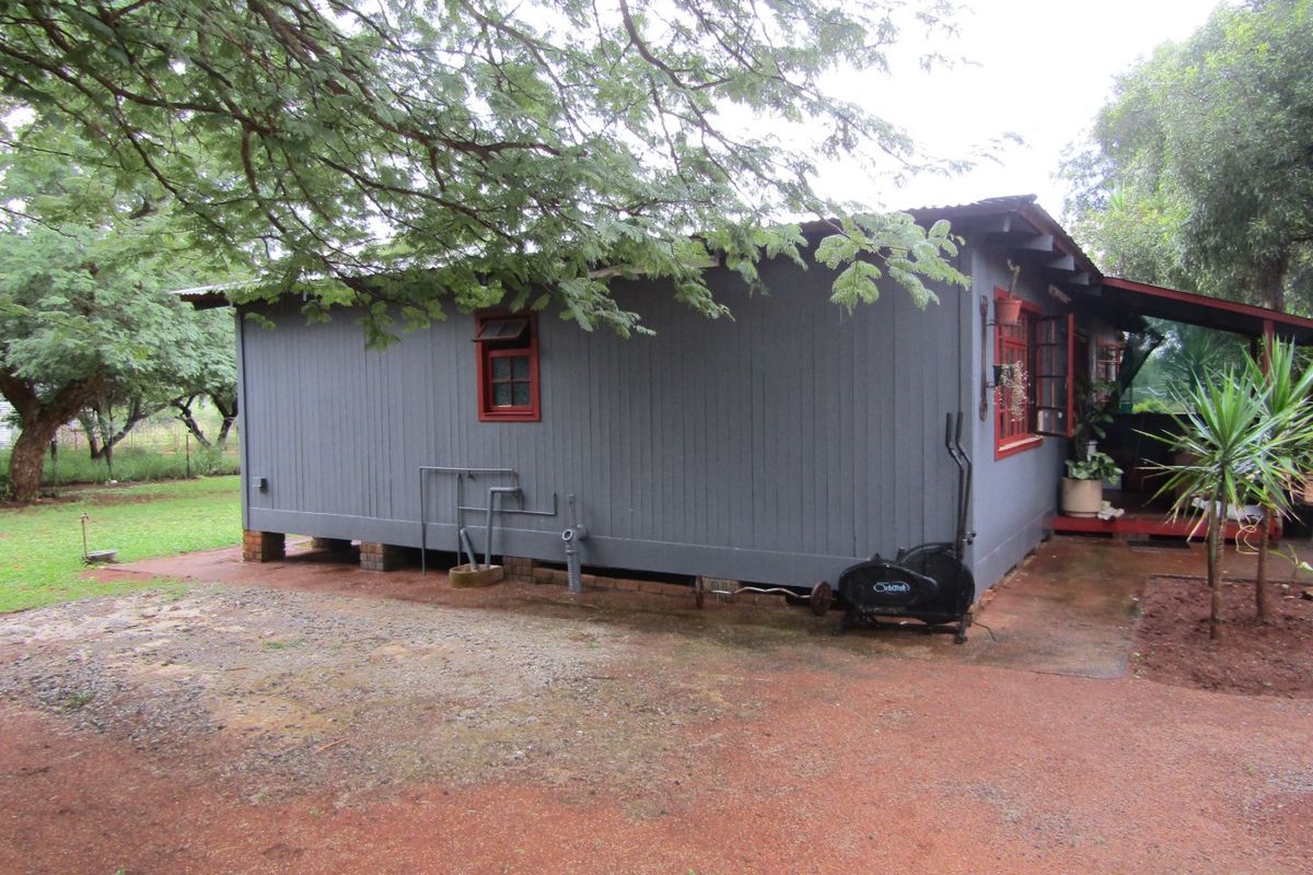 Rear view of a timber-clad farm cottage featuring a corrugated metal roof, casement windows, and a covered veranda area.
