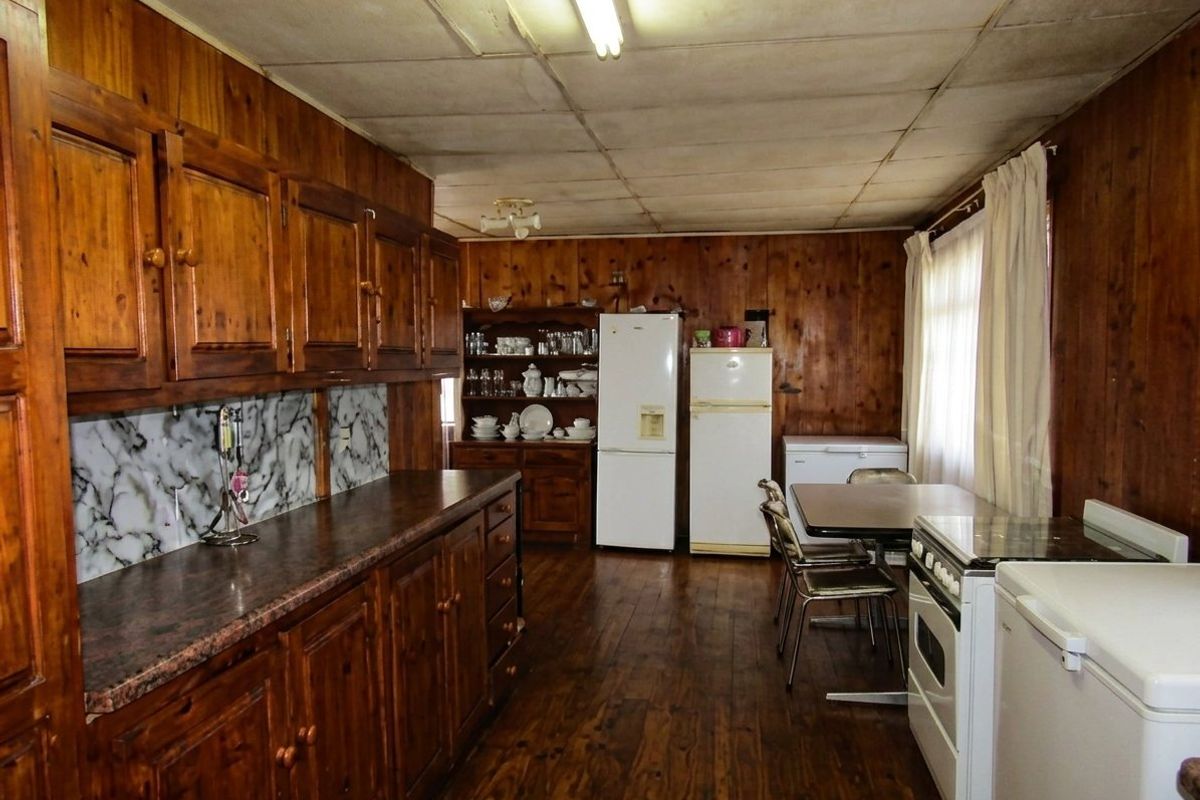 A rustic kitchen featuring extensive timber wall paneling, wooden cabinetry, and a functional layout with a freestanding stove and ample storage space.