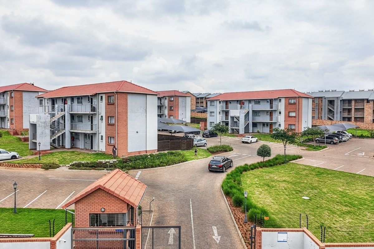 Aerial view of a residential townhouse complex featuring multiple apartment blocks, paved driveways, landscaped gardens, and a secure gated entrance.