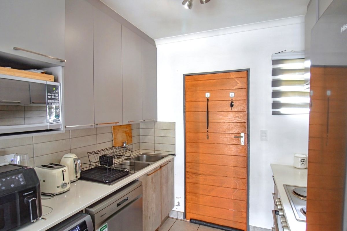 Compact kitchen featuring modern grey cabinetry, tiled backsplash, built-in microwave, integrated dishwasher, and a functional hob setup.