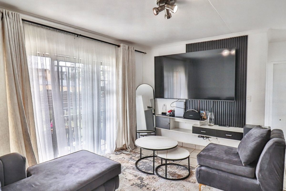 A well-maintained living room featuring modern slatted wall paneling, a built-in media console, tiled flooring, and a sliding glass door providing natural light.