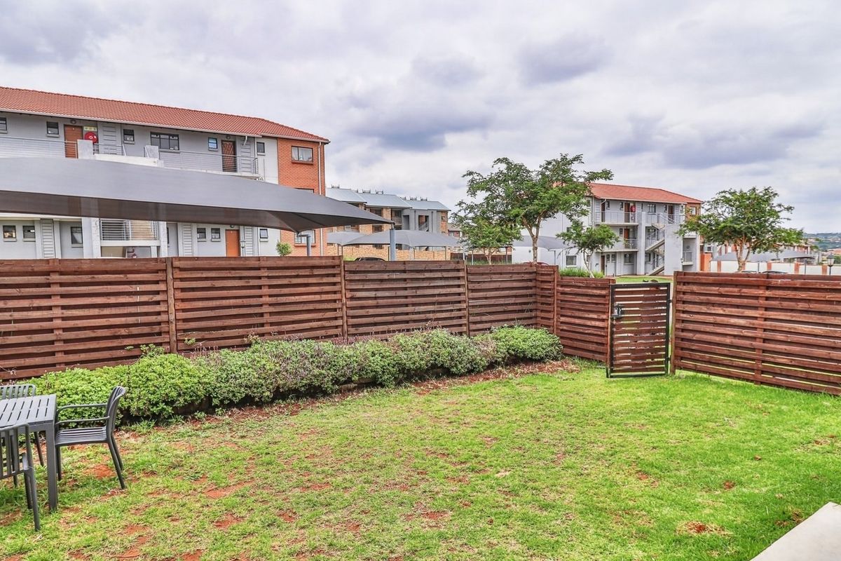 A private rear garden featuring a well-maintained lawn, timber slat fencing, and a shade sail, providing a functional outdoor space for the townhouse.