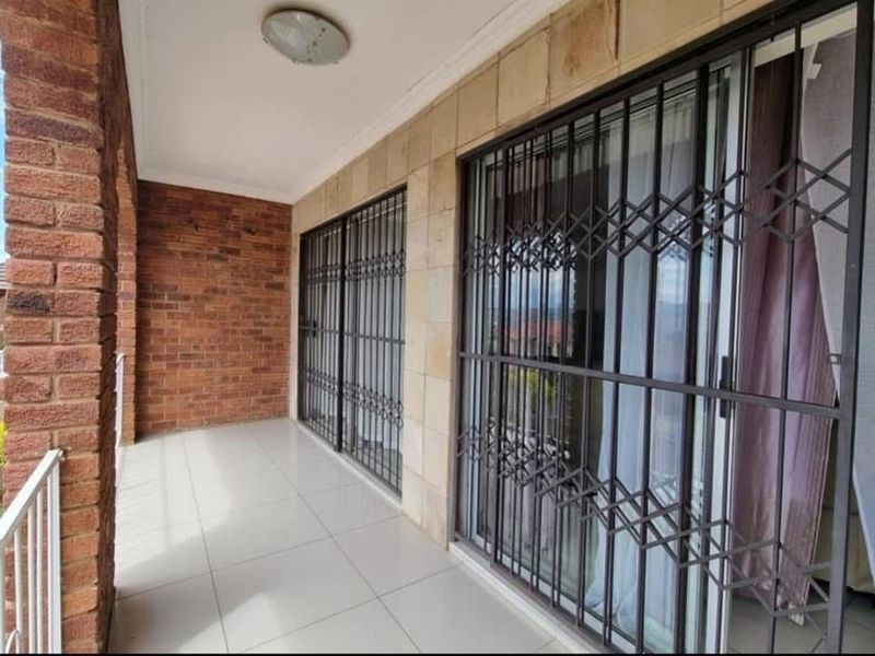 A covered patio featuring tiled flooring, exposed brickwork, and secure sliding glass doors with fitted metal security gates.