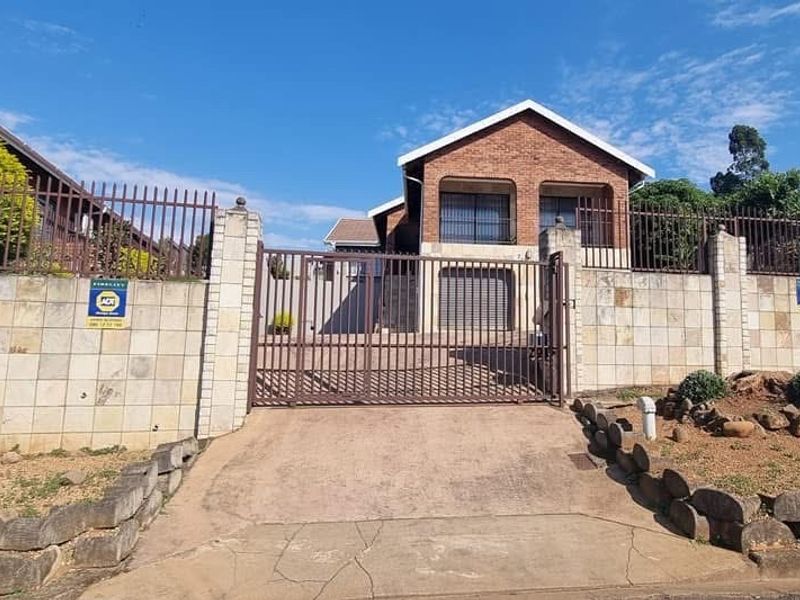 Front view of a brick house featuring a secure gated entrance, paved driveway, and perimeter walling with integrated security fencing.