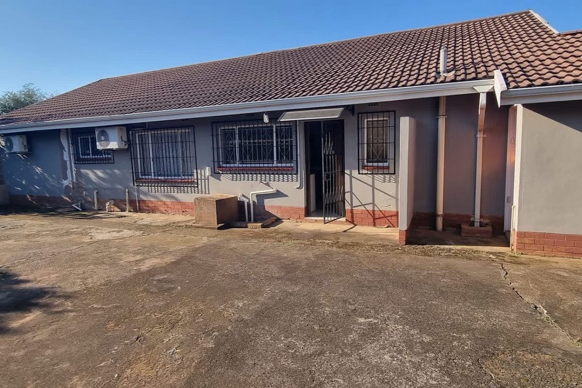 Rear exterior view of the house featuring a concrete patio area, tiled roof, and security bars on windows.