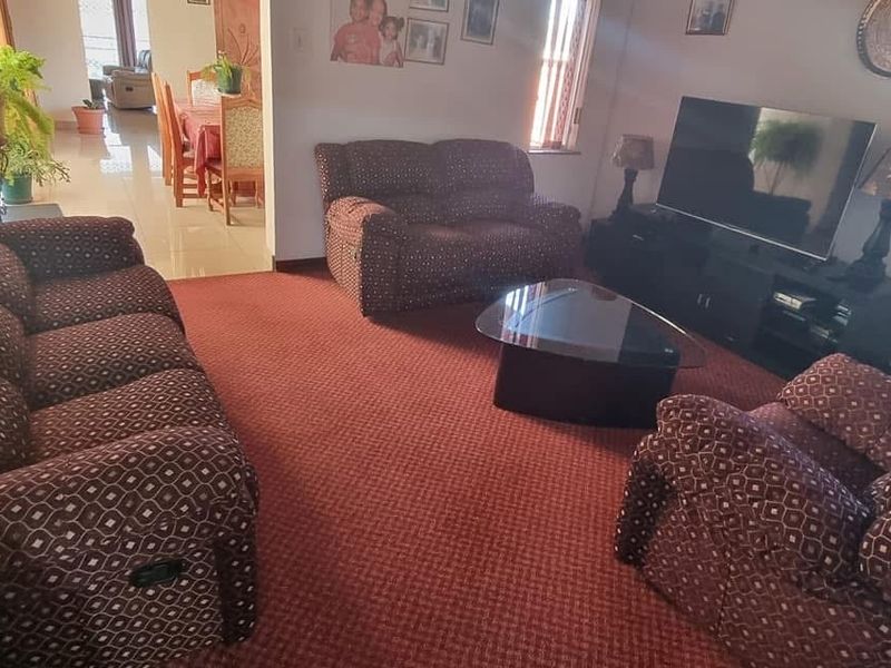 A spacious living room featuring wall-to-wall carpeting, with an open-plan layout leading into the adjacent dining area.