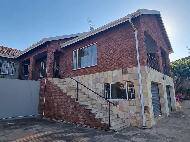 Exterior view of a multi-level brick house featuring a raised staircase, stone-clad lower level, double garage, and security fencing.
