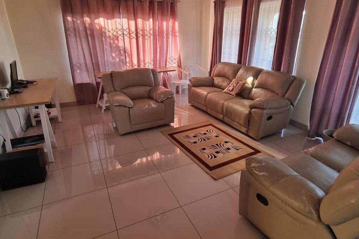 A spacious living room featuring large format floor tiles, expansive windows with curtains, and direct access to an outdoor balcony area.
