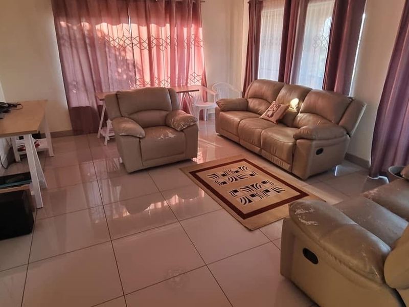 A spacious living room featuring large format floor tiles, expansive windows with curtains, and direct access to an outdoor balcony area.