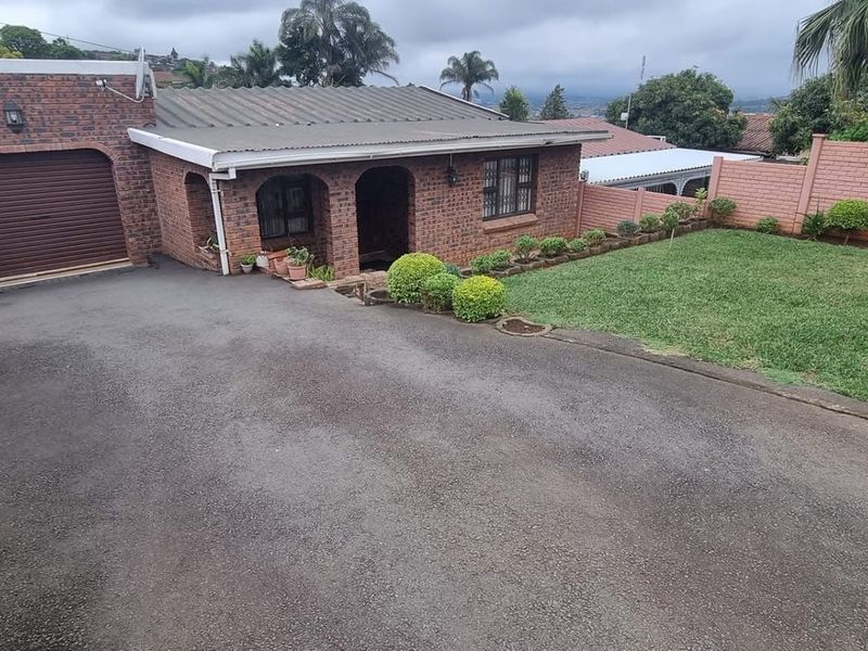 Front view of a brick-faced house featuring a single garage, paved driveway, and a landscaped front garden enclosed by perimeter walls.