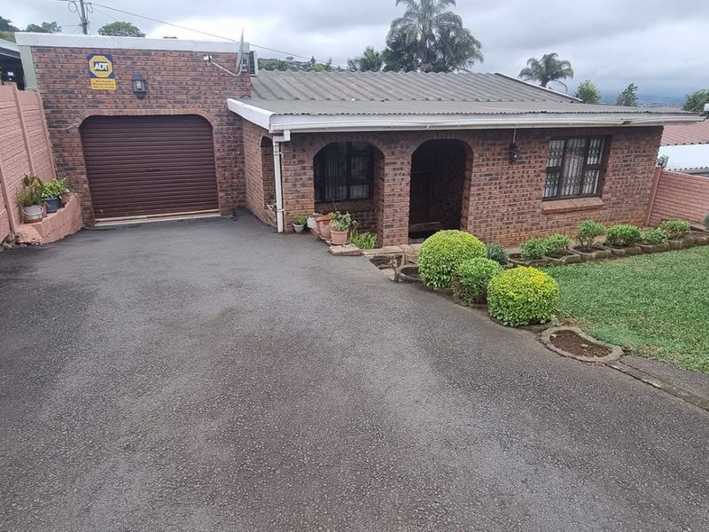 Front exterior view of a face-brick house featuring a paved driveway, single garage, covered entrance, and a well-maintained front lawn with boundary walls.