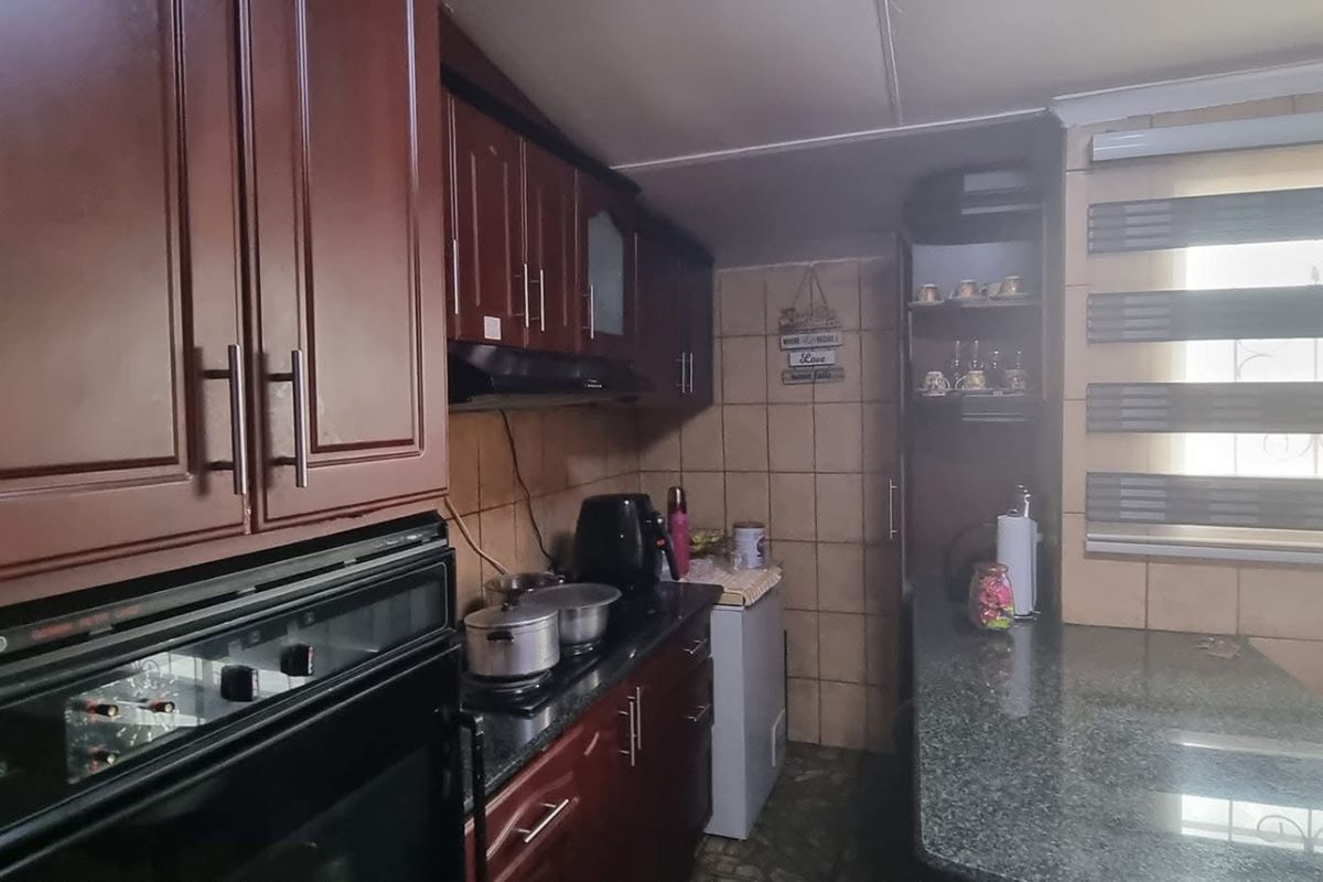 A functional kitchen featuring dark wood cabinetry, granite countertops, a built-in oven, and a breakfast bar area with tiled walls.