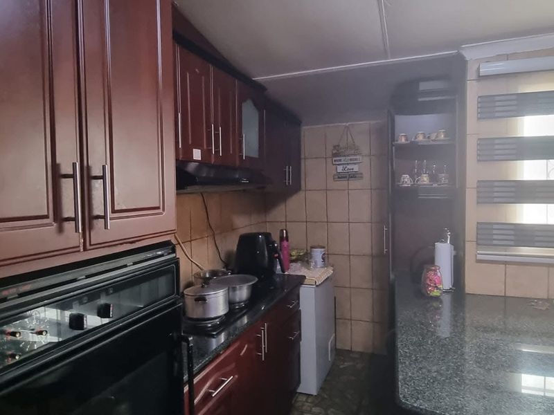 A functional kitchen featuring dark wood cabinetry, granite countertops, a built-in oven, and a breakfast bar area with tiled walls.