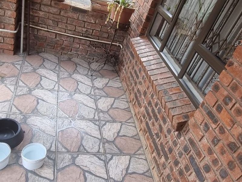 A covered patio area featuring exposed brickwork, arched architectural detailing, and decorative stone-look floor tiling.