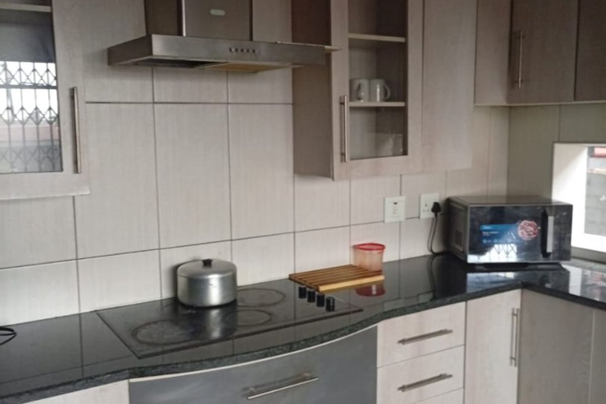 A functional kitchen featuring light-toned cabinetry, dark granite countertops, a built-in electric hob, and a stainless steel extractor fan with tiled backsplash.
