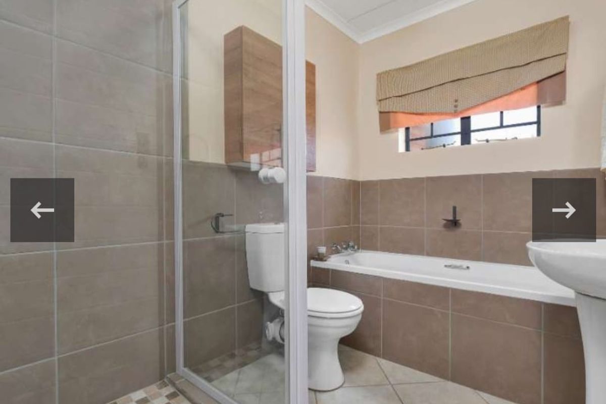 A functional bathroom featuring a shower enclosure, bathtub, pedestal basin, and wall-mounted storage cabinet with neutral wall and floor tiling.