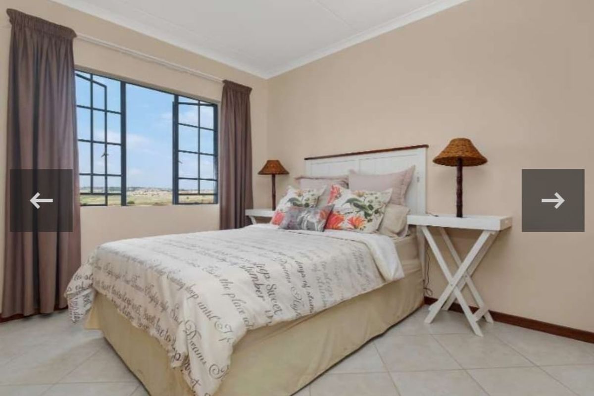 A well-lit bedroom featuring neutral wall tones, tiled flooring, and a large casement window providing natural light.