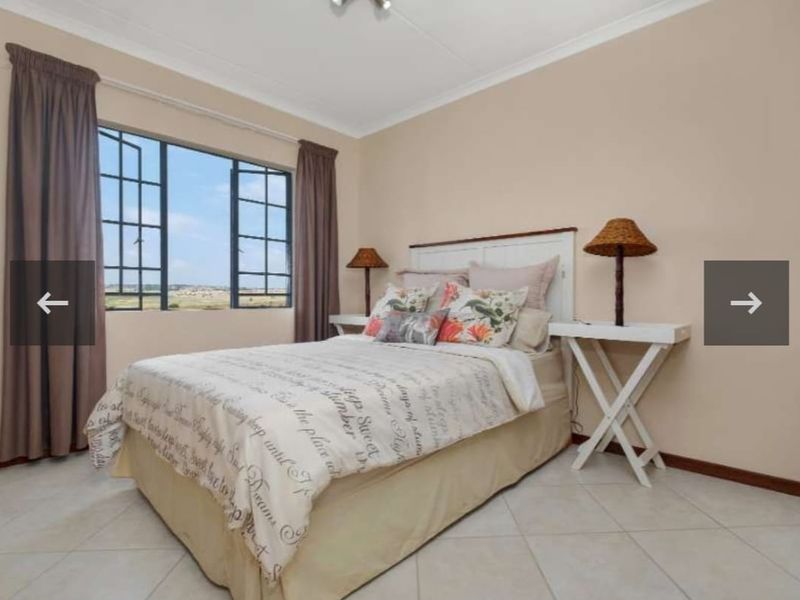 A well-lit bedroom featuring neutral wall tones, tiled flooring, and a large casement window providing natural light.