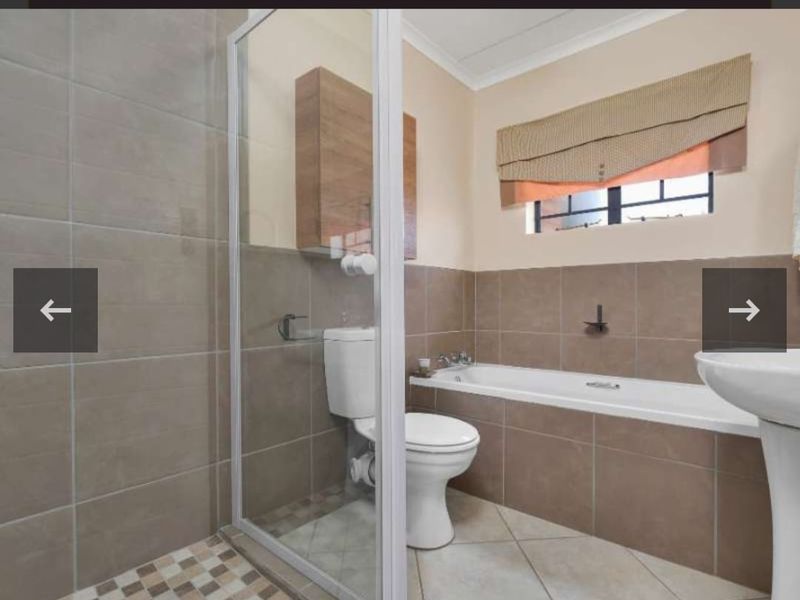 A functional bathroom featuring a shower enclosure, bathtub, pedestal basin, and wall-mounted storage cabinet with neutral wall and floor tiling.