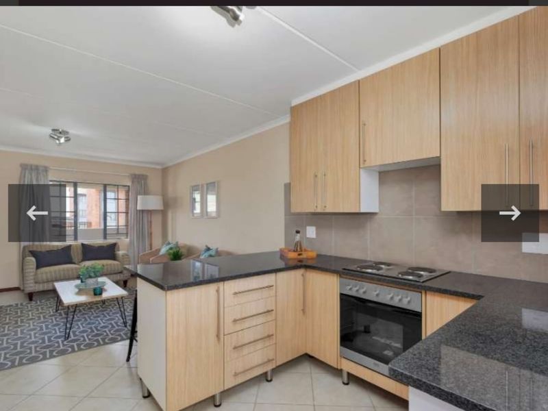 Open-plan kitchen and living area featuring light wood cabinetry, granite countertops, built-in oven and hob, and neutral tiled flooring.