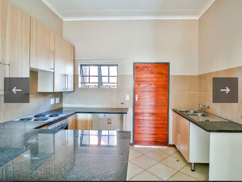 A functional kitchen featuring light wood cabinetry, granite countertops, an electric hob, and a double basin sink with tiled splashbacks.