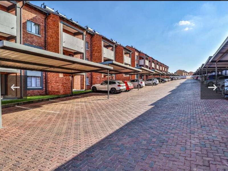 Exterior view of an apartment complex featuring a paved driveway with multiple covered parking bays and brick building facades.