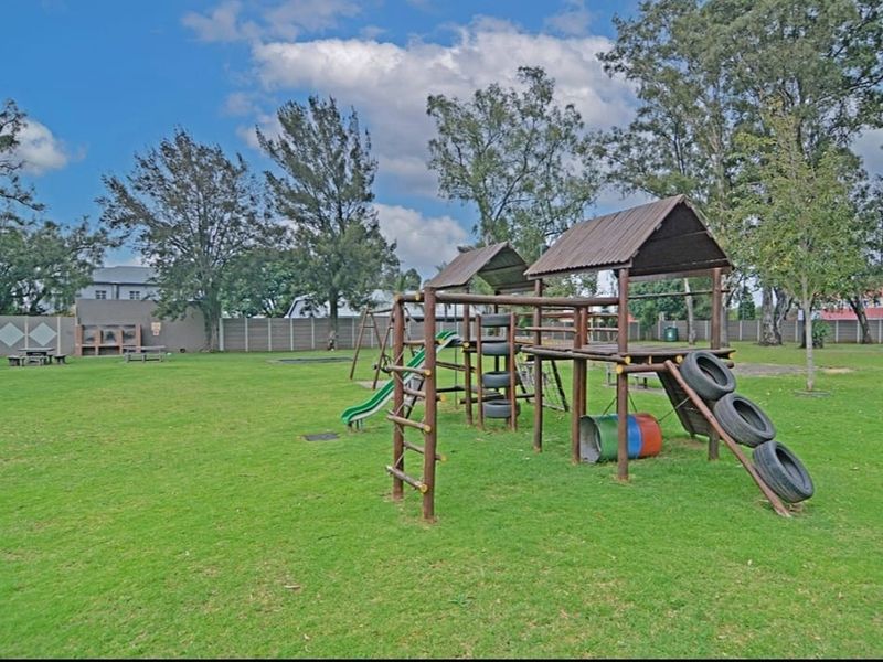 Spacious communal garden area featuring a wooden playground structure, manicured lawn, and a built-in braai facility for outdoor entertainment.