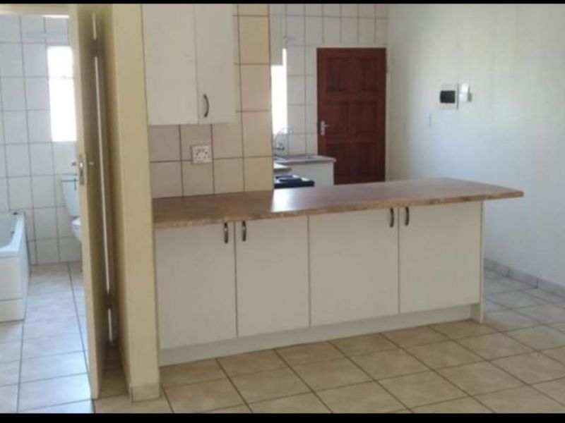 Open plan kitchen area with laminate countertops and white cabinetry, adjacent to a tiled bathroom featuring a built-in bathtub and toilet.