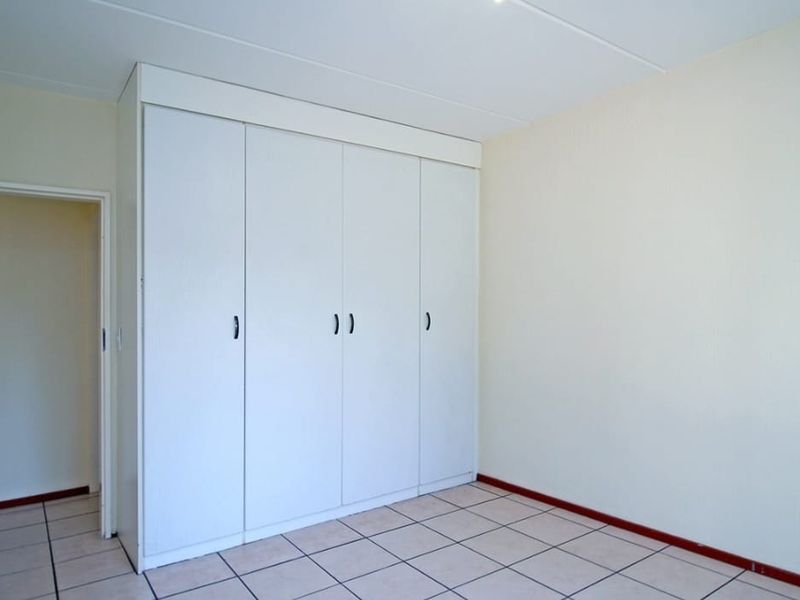 A bright, empty bedroom featuring neutral walls, tiled flooring, and ample built-in cupboard storage.