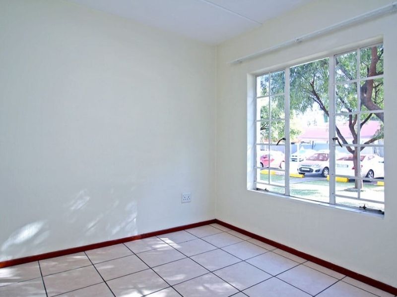 A bright, empty bedroom featuring neutral walls, tiled flooring, and a large window with security bars overlooking the exterior.