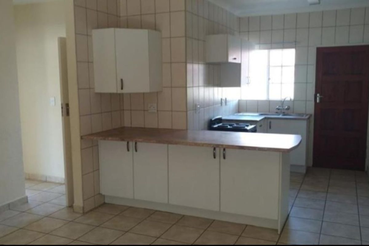 A functional kitchen featuring white built-in cabinetry, laminate countertops, tiled backsplash, and tiled flooring in a clean, empty space.