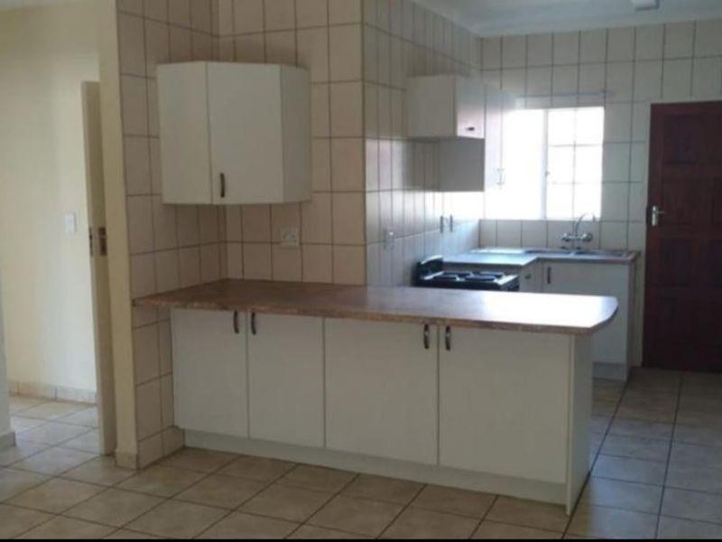 A functional kitchen featuring white built-in cabinetry, laminate countertops, tiled backsplash, and tiled flooring in a clean, empty space.