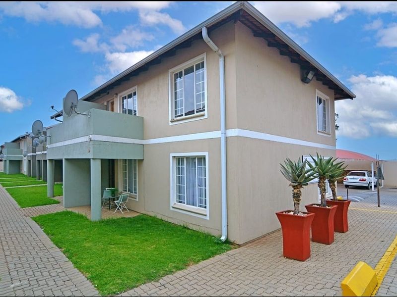 A view of the apartment complex exterior featuring a paved driveway, ground floor patio, and upper-level balcony with satellite dish installations.