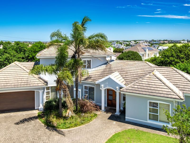 A well-maintained suburban house featuring a tiled roof, paved driveway, double garage, and a covered entrance with decorative columns.
