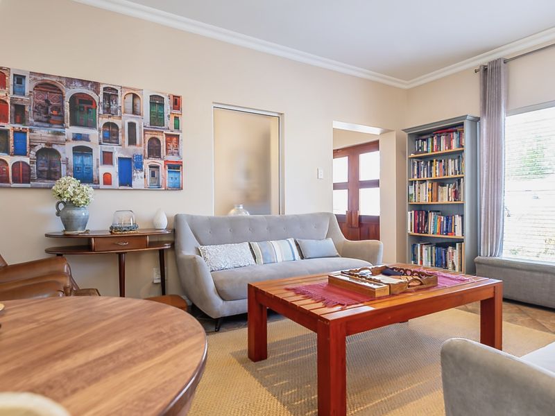 A well-maintained living room featuring neutral walls, coving, built-in shelving, and large windows that provide ample natural light.