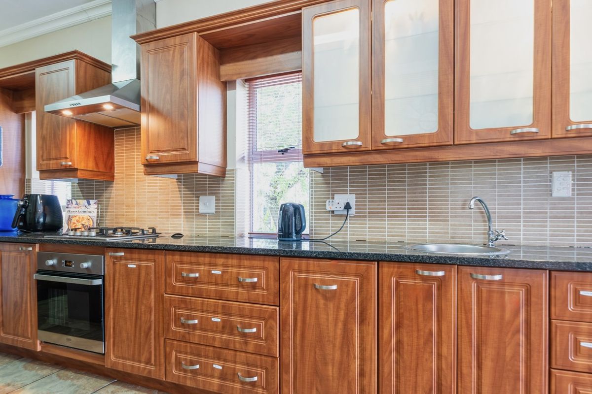A well-maintained kitchen featuring warm-toned wooden cabinetry, granite countertops, a stainless steel oven, gas hob, and a tiled backsplash.
