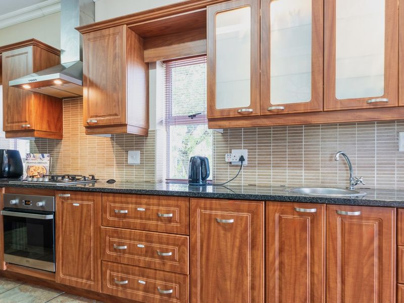 A well-maintained kitchen featuring warm-toned wooden cabinetry, granite countertops, a stainless steel oven, gas hob, and a tiled backsplash.