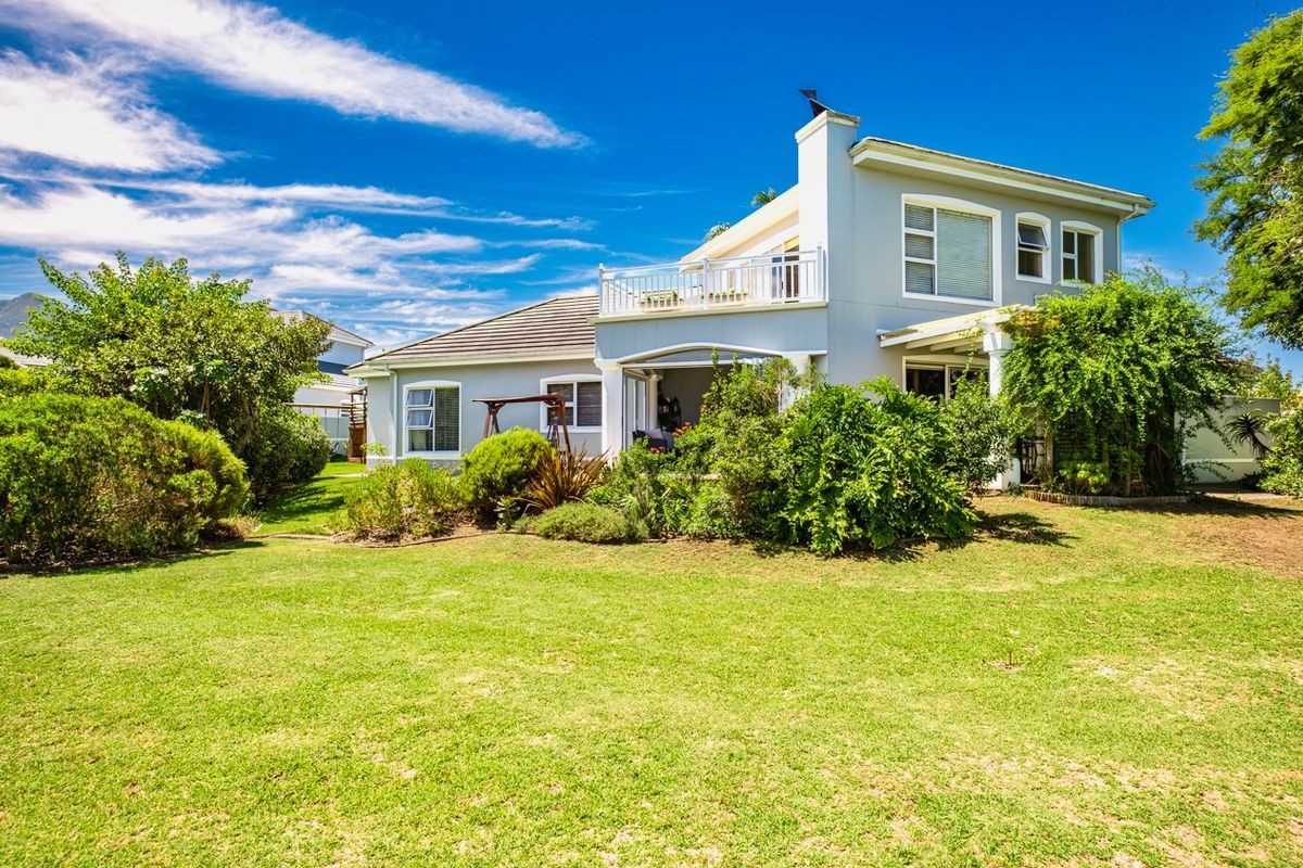 Rear view of a two-story house featuring a spacious lawn, landscaped garden, and an upper-level balcony.