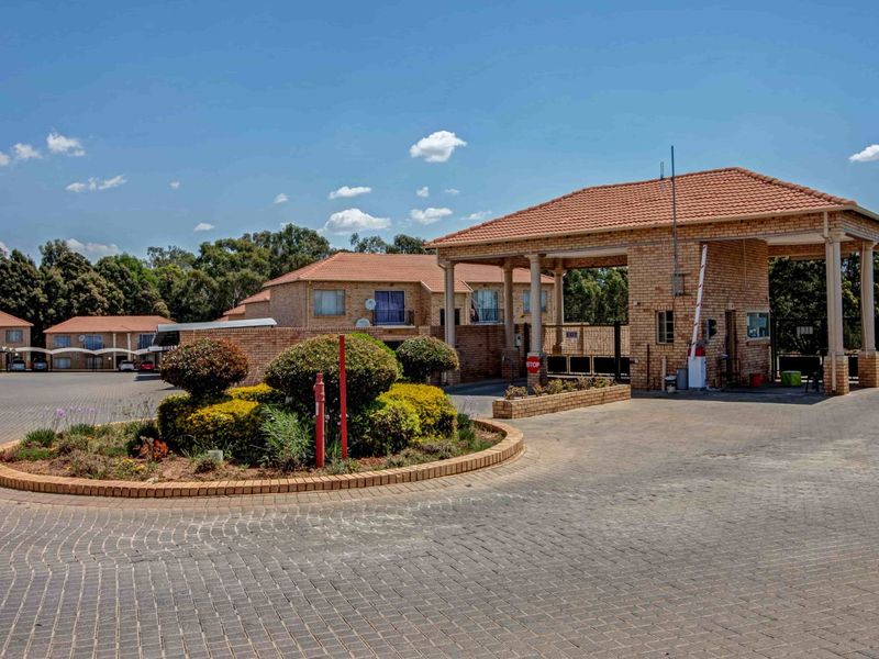 A view of the apartment complex entrance featuring a brick security gatehouse, paved driveway, and landscaped garden beds.