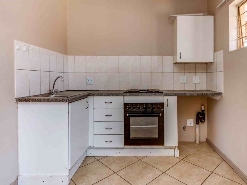 A compact kitchen featuring built-in cabinetry, a stainless steel sink, an integrated oven and hob, and tiled finishes throughout.