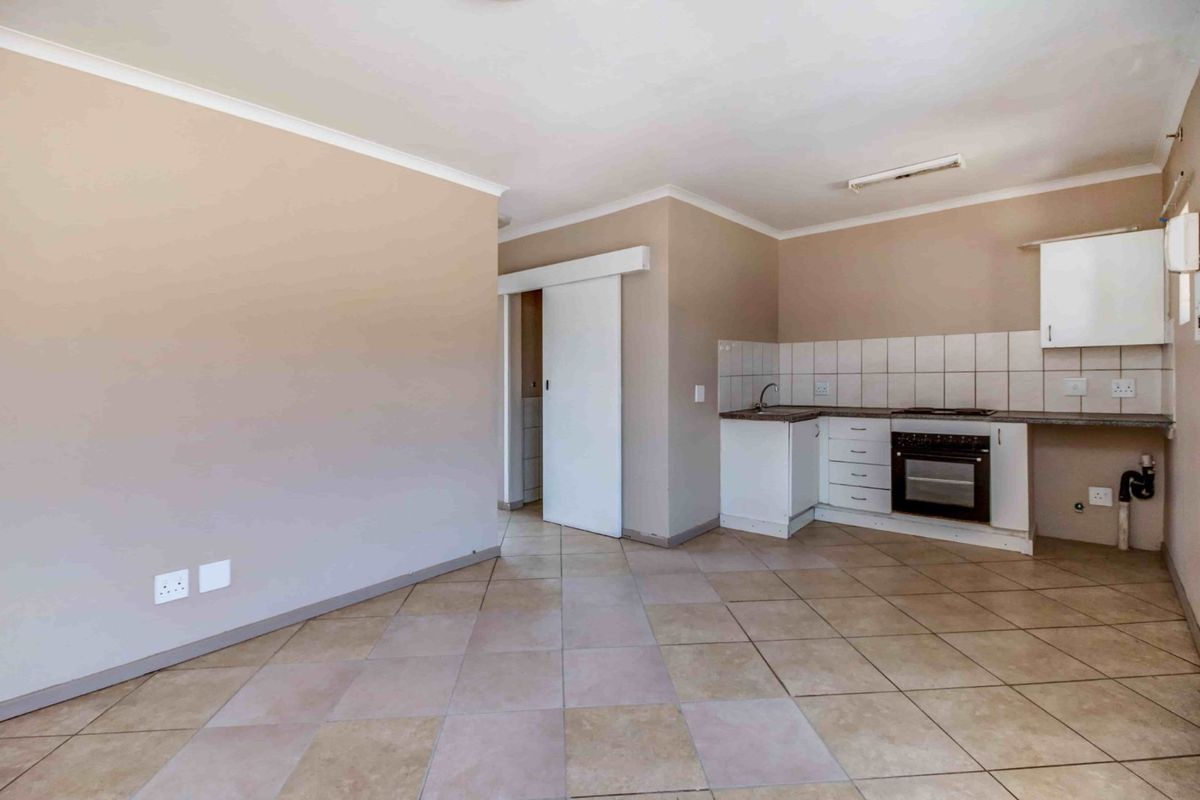 Open plan living area featuring a compact kitchen with built-in oven, hob, and tiled flooring throughout.